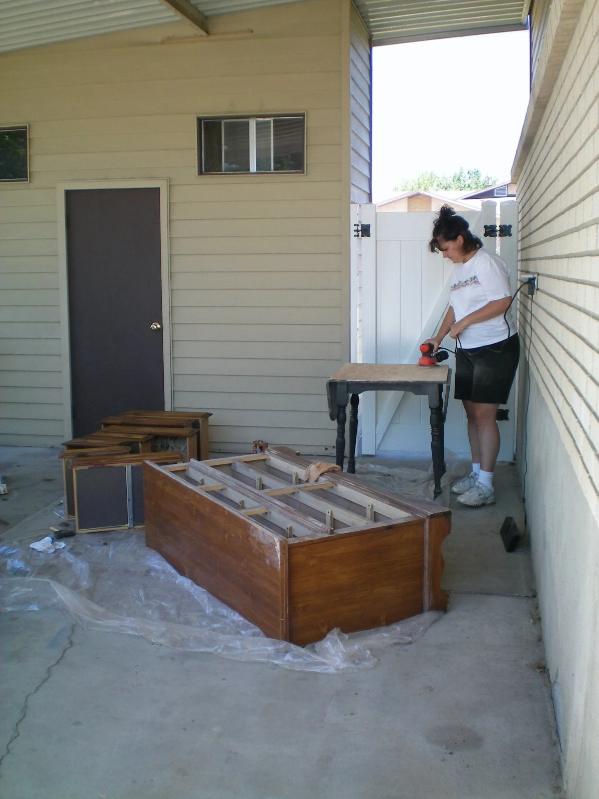 Diana sanding the dresser frame on the patio outside, with the drawers removed and the carcass lying on plastic sheeting