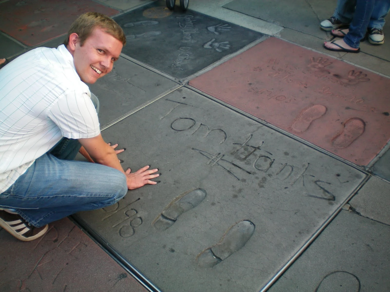Jon crouching down with his hand placed next to Tom Hanks' handprints and signature cast in the cement at Grauman's Chinese Theatre