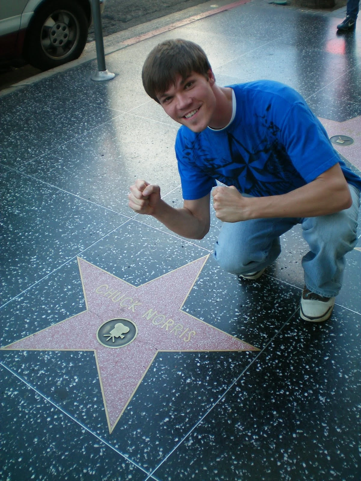 Devin crouching with both fists raised next to Chuck Norris's star on the Hollywood Walk of Fame, grinning at the camera