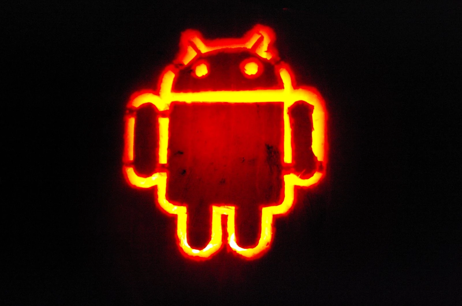 Jon's carved pumpkin lit from inside, glowing orange-red against a black background in the shape of the Android robot logo