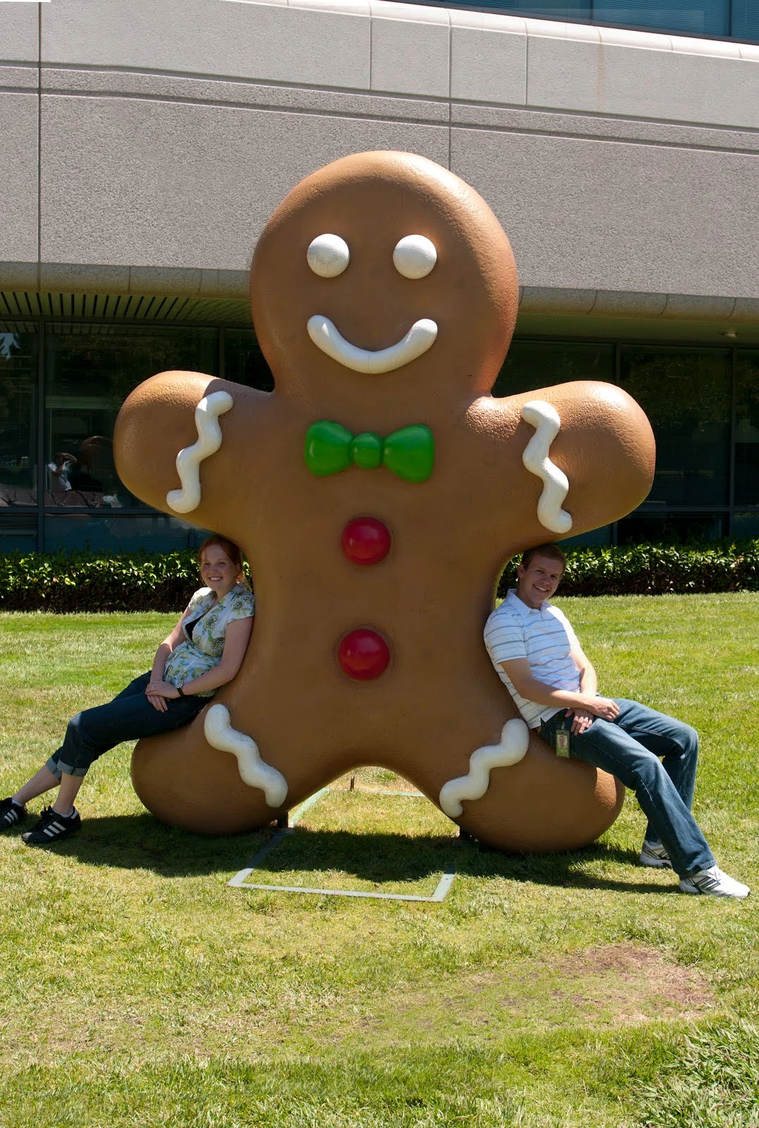 Danielle and Jon seated on either side of the giant Android Gingerbread Man statue on Google's campus lawn, with the Googleplex building visible in the background