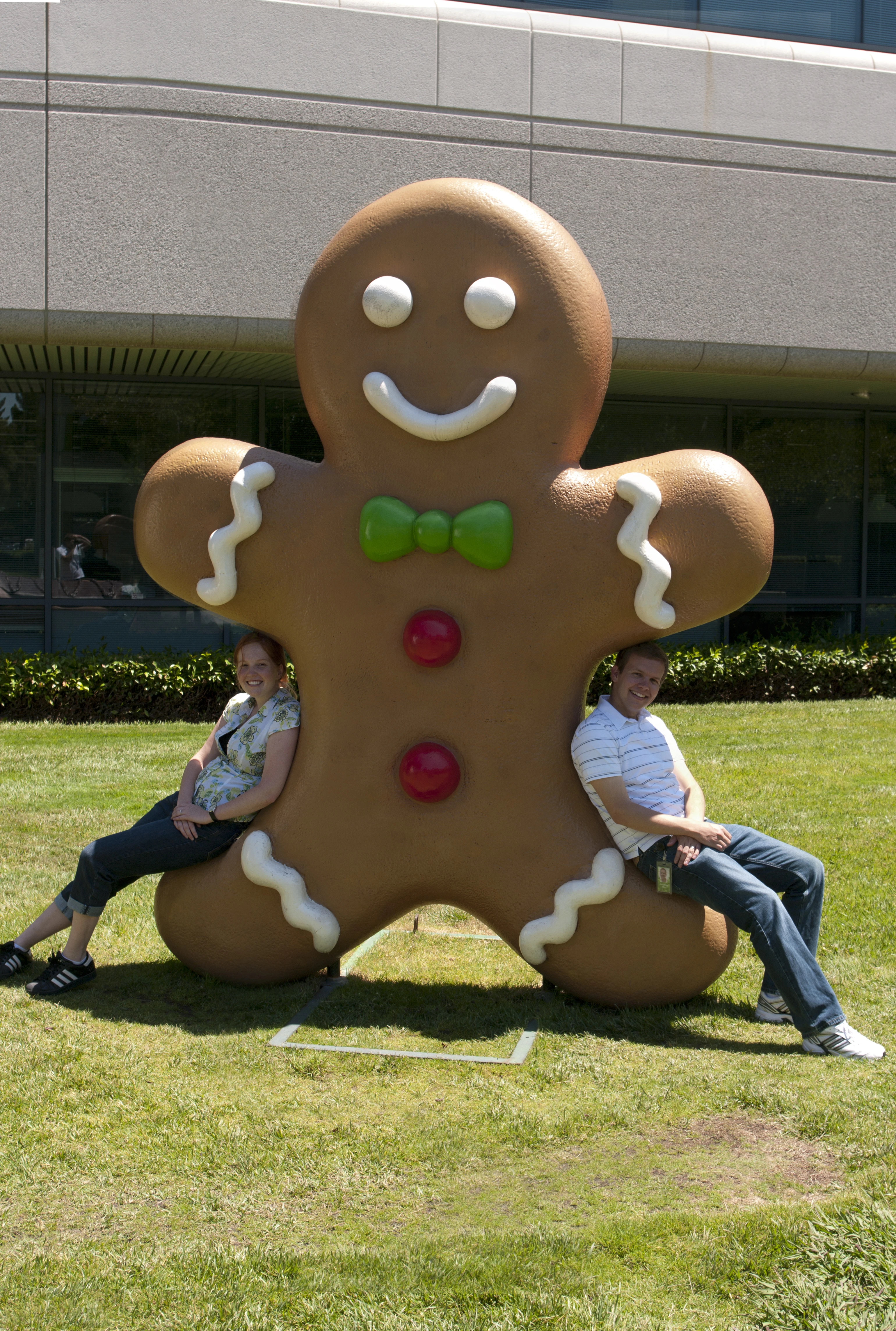 Jon and Danielle people seated on either side of the giant Android Gingerbread Man statue on the Google campus lawn, leaning against its feet